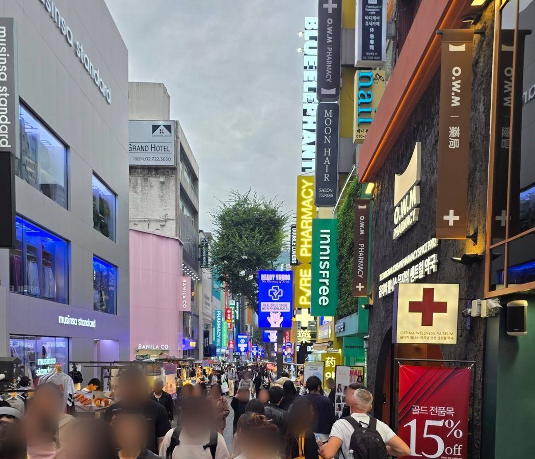 명동 중앙로, 해 질 무렵. 거리 양쪽으로 약국 간판이 줄지어 있습니다.