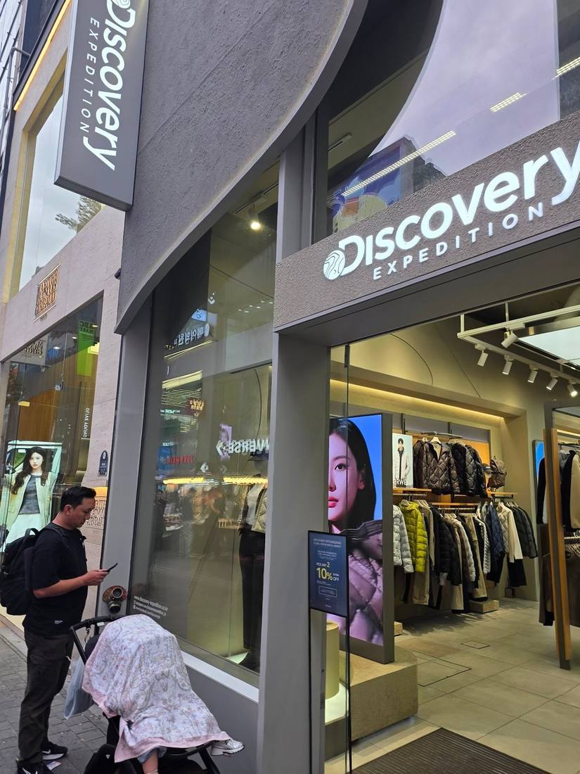 디스커버리 익스페디션 매장. 입구에 ‘DISCOVERY MYEONGDONG — GLOBAL VISITOR SPECIAL BENEFIT, PICK ANY 2 · 10% EXTRA OFF’ 안내판이 보입니다.